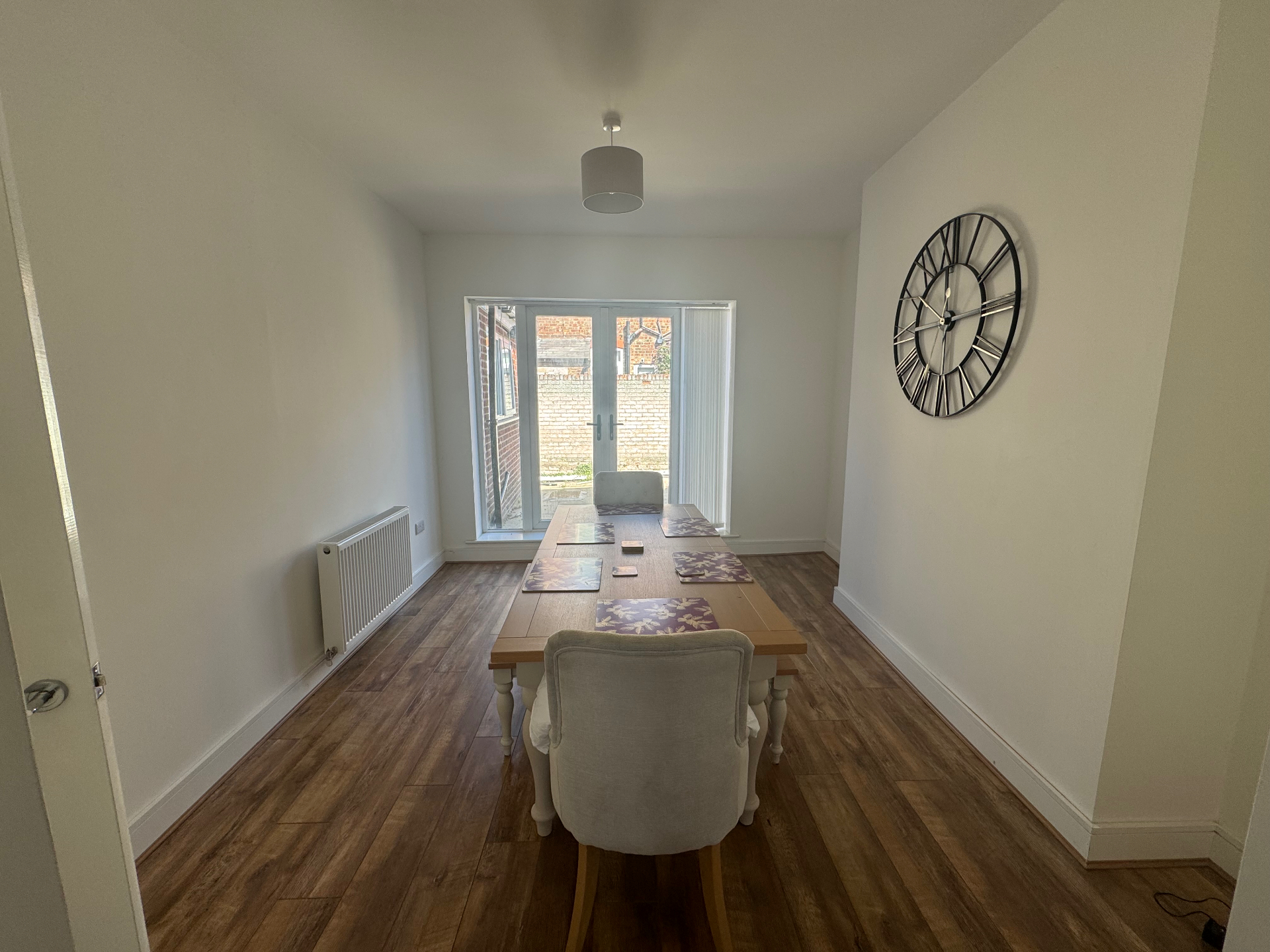 A dining and social room with a large wooden table, seating for the household and doors onto the rear of the home