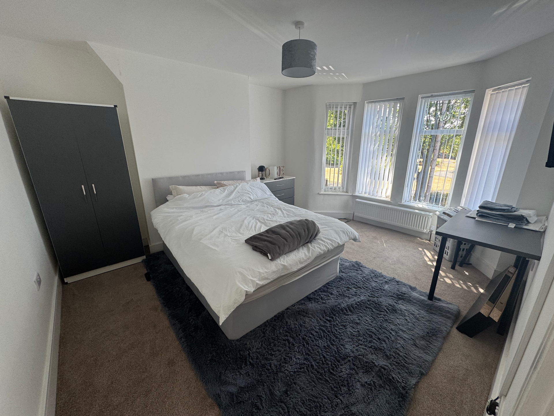 A spacious, light single bedroom with a bed, wardrobe, chest of drawers, desk and large windows